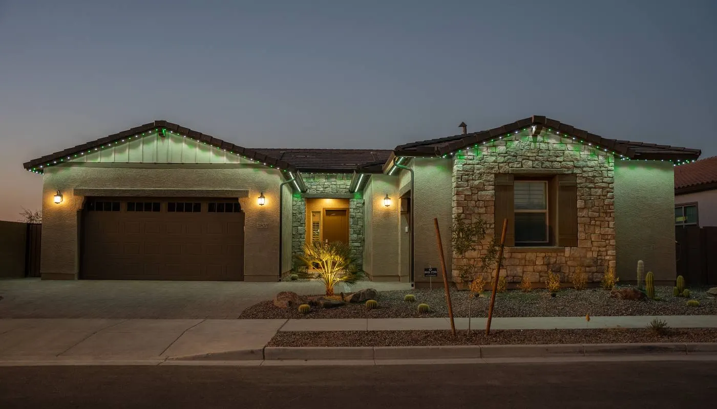 Stone and stucco desert home lit in green and white permanent LED lighting along the roofline and garage