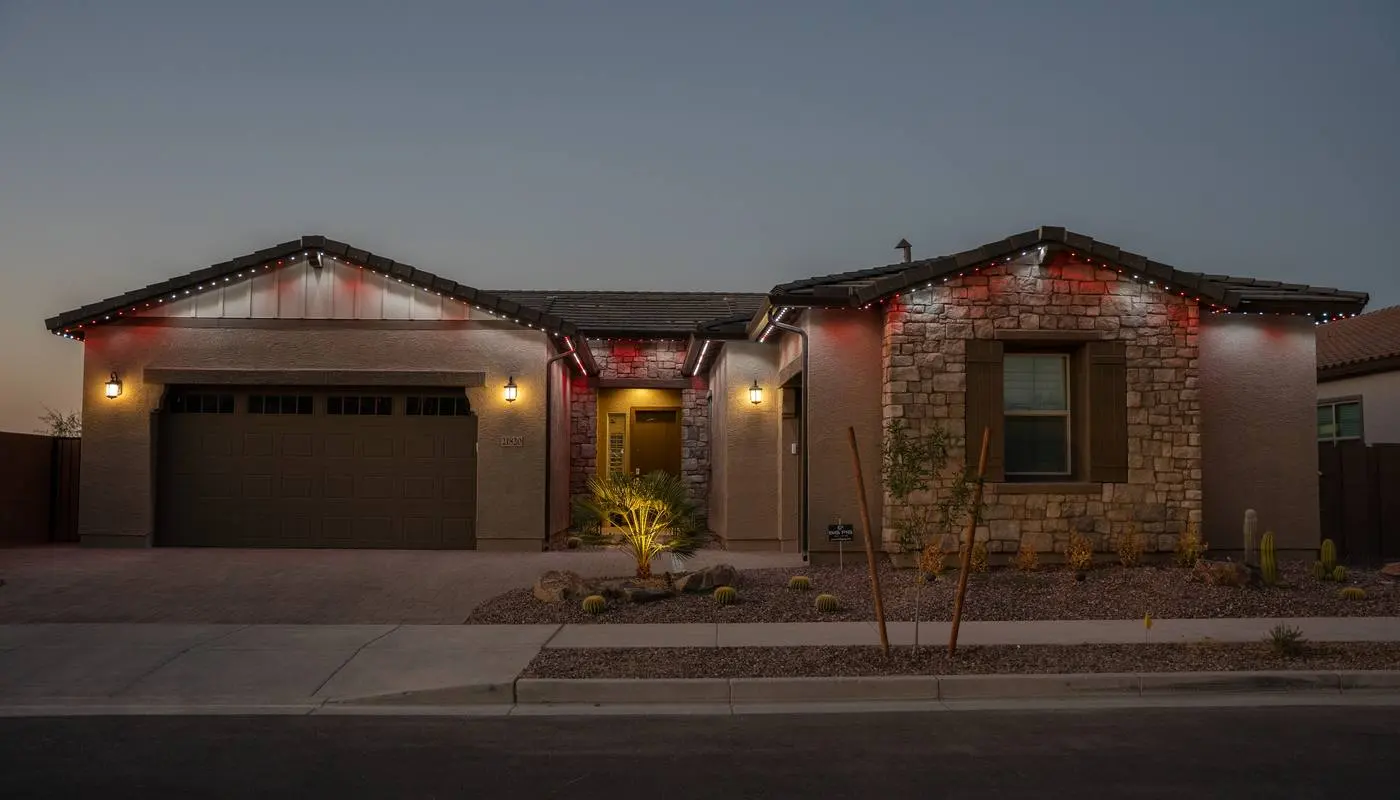 Desert home at dusk with alternating red and white permanent roofline lighting and warm uplighting on the stone facade