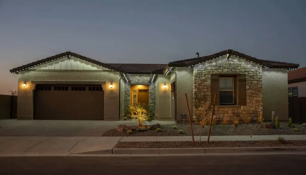 Single-story desert home at dusk with warm white permanent LED lighting along the roofline, garage, and stone entry