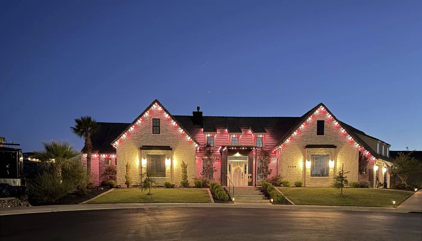 Large brick ranch home at night with pink and warm white permanent lighting outlining steep gables
