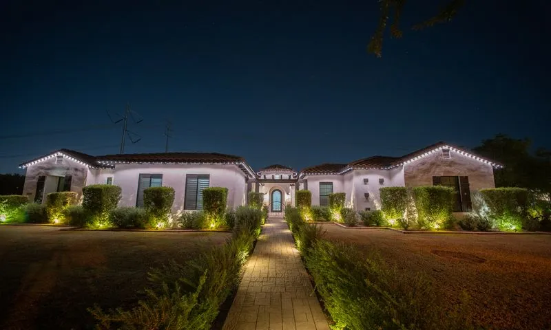 Spanish-style home at night with crisp white permanent roofline lighting and green landscape uplighting