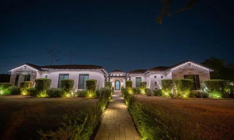 Spanish-style home at night with crisp white permanent roofline lighting and green landscape uplighting on trimmed hedges